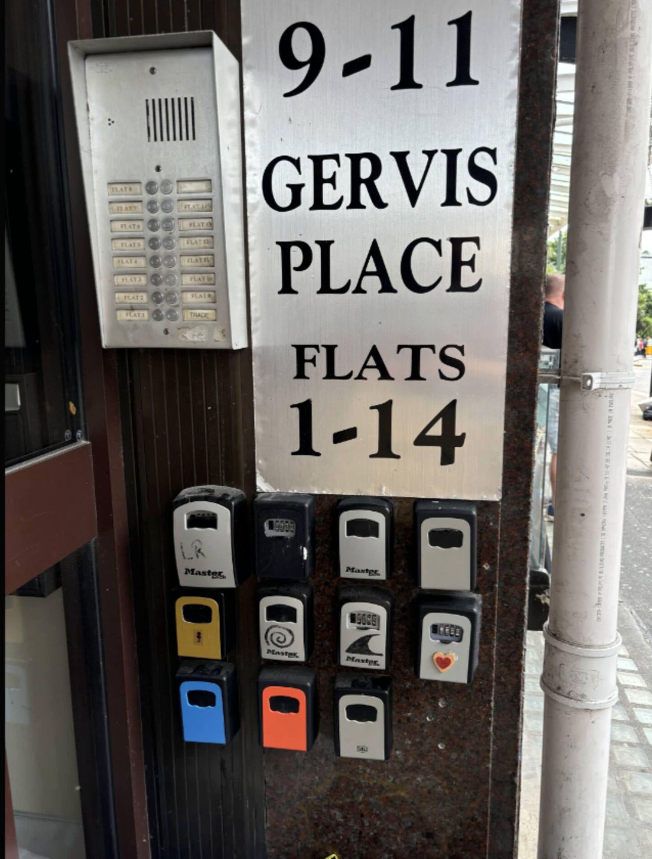 Indicador que mostra '9-11 GERVIS PLACE FLATS 1-14', amb un comptador de pàrquing i un dispositiu de teclet a sota.