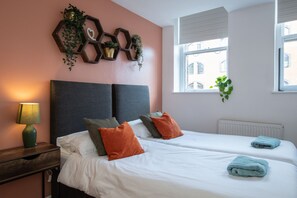 Ett hotellrum med två sängar, ett nattduksbord, en lampa, ett fönster med persienner och en väggdekoration.