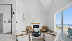 Une pièce avec une télévision, deux fauteuils, une petite table basse et une vue sur la plage.