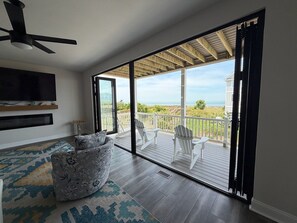 A spacious living room with a large sliding glass door leading to a deck with a view of the ocean. - Norfolk Family Beach House 5BR Walk To Sand • Ideal for Groups of 10! (Norfolk)