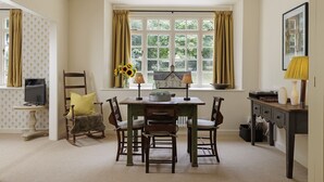 A dining area with a wooden table and chairs, a window with curtains, a small lamp, and a television on a stand. - Beautifully presented dog friendly - The Coach House at Broadwell Manor (Broadwell)