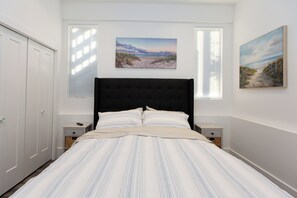 A bedroom with a large bed, two bedside tables, a wardrobe, and two wall-mounted paintings.