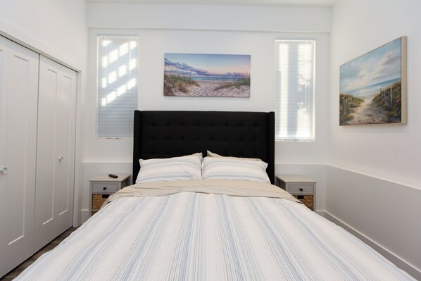 A bedroom with a large bed, two bedside tables, a wardrobe, and two wall-mounted paintings. - Sidney Solace – 1BR Suite Minutes from Waterfront (Sidney)