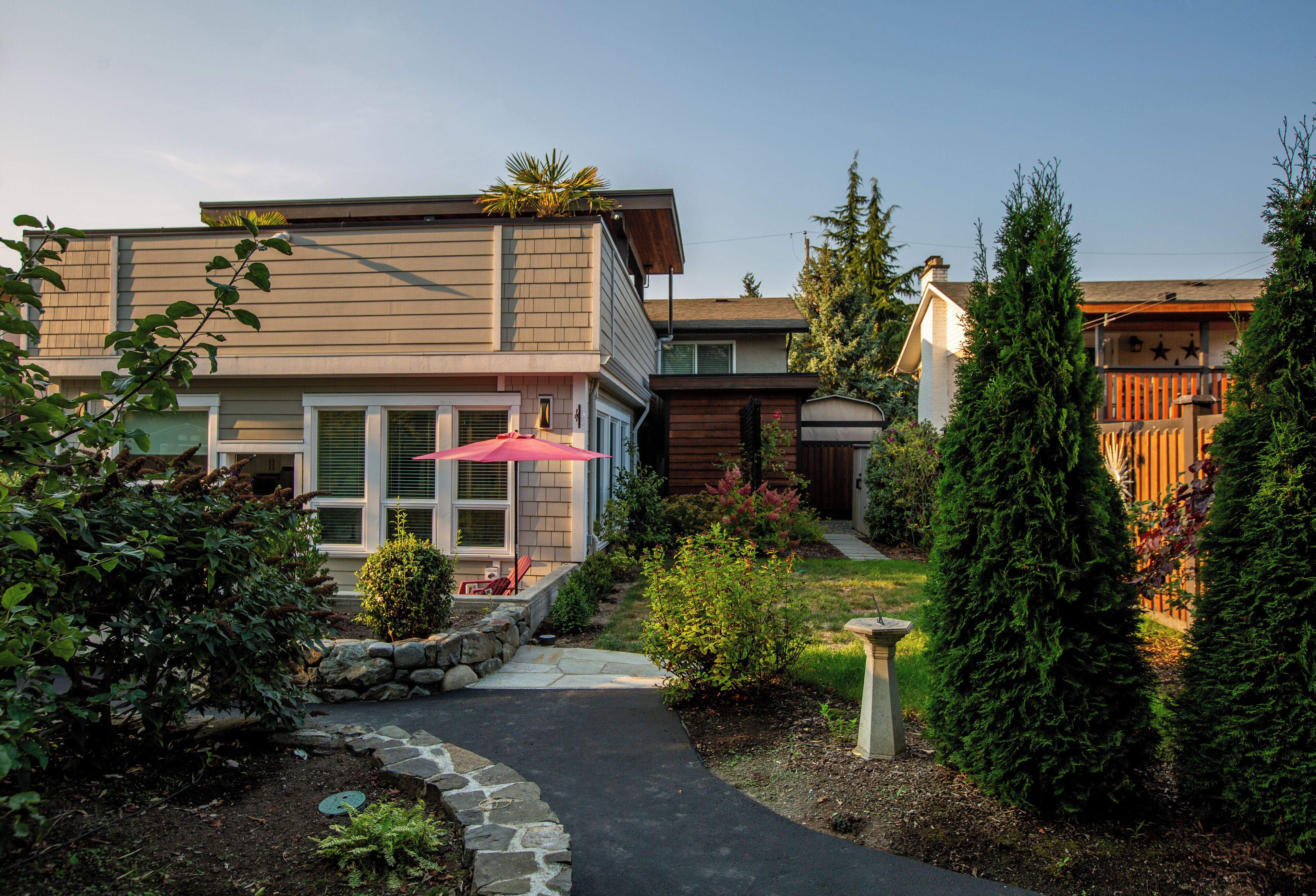 A modern two-story house with a stone pathway leading to the front door, surrounded by well-maintained gardens and tall evergreen trees.