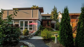 Une maison moderne à deux étages, avec un chemin de pierre menant à la porte d’entrée, entourée de jardins bien entretenus et de grands arbres à feuilles persistantes.