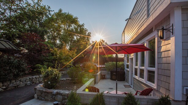 Une terrasse avec un parasol rouge, un bac à fleurs en pierre et des sièges d’extérieur.