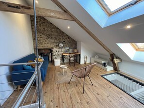 A loft-style room with a sloped ceiling, stone wall, wooden beams, a blue sofa, a wicker chair, and a skylight. - A retreat at the foot of the Pyrenees; house near Lourdes; pets welcome (Juillan)