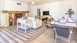Een moderne woonkamer met een open haard, een eethoek met een tafel gedekt voor vier personen, en een aan de muur bevestigde televisie.