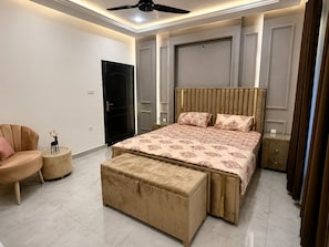 A bedroom with a bed, a chair, a bench, a ceiling fan, and a door.
