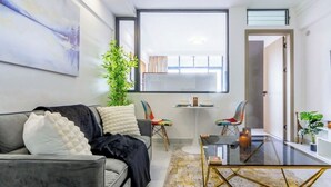 A modern living room with a grey sofa, a glass coffee table, and a view of a dining area through a large window. - Stylish| 2 Beds| Fast Wifi| Best Area| (Nairobi)