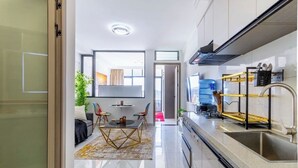 A modern kitchen with a built-in oven, a sink, and a water dispenser. There is a dining area with a table and chairs, and a view of the city through large windows. - Stylish| 2 Beds| Fast Wifi| Best Area| (Nairobi)