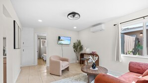A modern living room with a beige sofa, a red sofa, a round wooden coffee table, and a TV mounted on the wall.