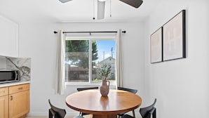 A modern kitchen with a round wooden table, black chairs, a microwave, and a window with curtains.
