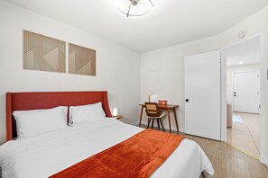 Hotellihuoneessa on sänky, työpöytä ja tuoli. Huoneesta on ovi toiseen huoneeseen.