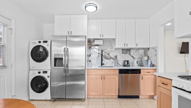 A modern kitchen with stainless steel appliances, marble backsplash, and light wood cabinets.