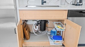 A kitchen with a built-in dishwasher, a sink, and a storage cabinet with cleaning supplies.