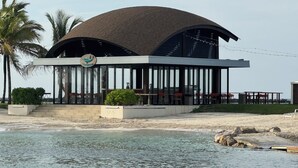 Un restaurante moderno frente al mar, con techo curvo, terraza al aire libre y vistas al océano.