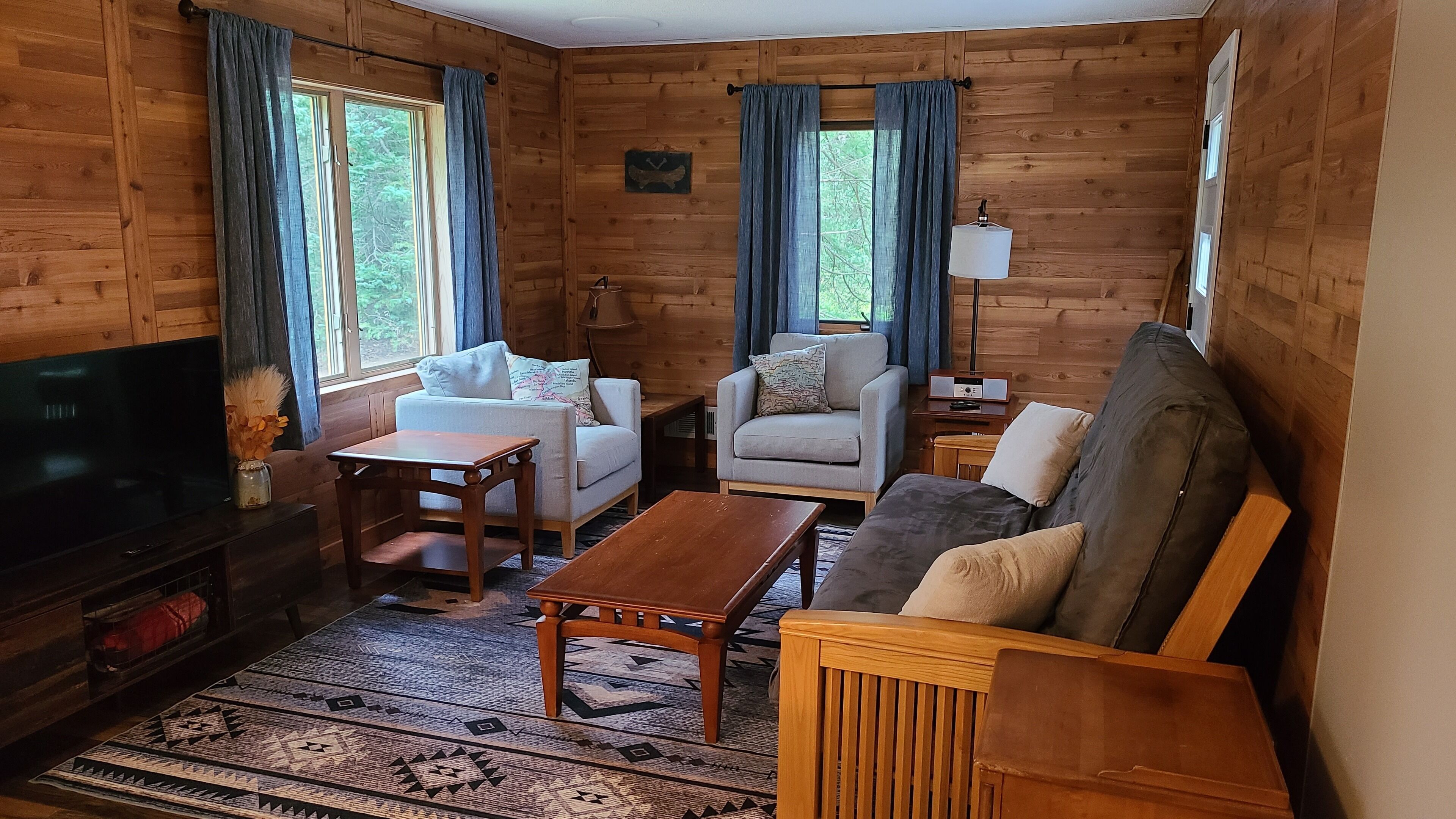 L’intérieur d’un chalet accueillant, avec un canapé, un fauteuil et un téléviseur posé sur un meuble en bois.