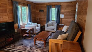 Un interior acogedor de cabaña con un sofá, un sillón y un televisor sobre un soporte de madera.
