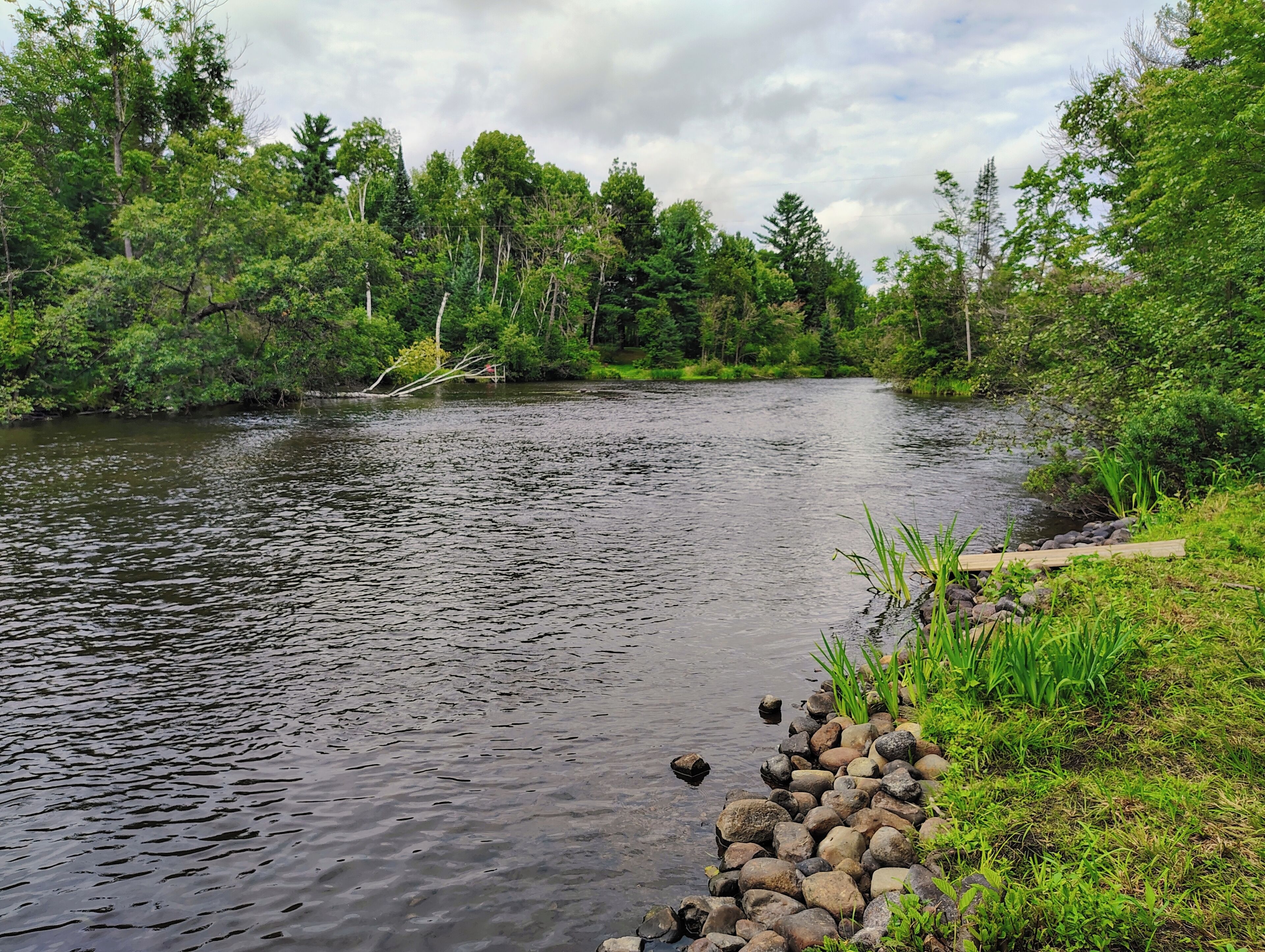 Une rivière dont les berges sont rocheuses et bordée d’une végétation luxuriante de chaque côté.