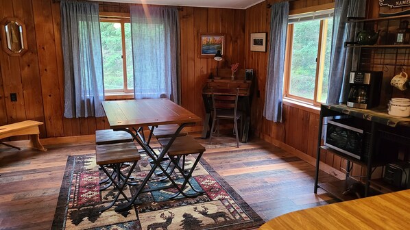 Un interior de madera con una mesa de comedor, bancos, una alfombra y una cocina con estufa.