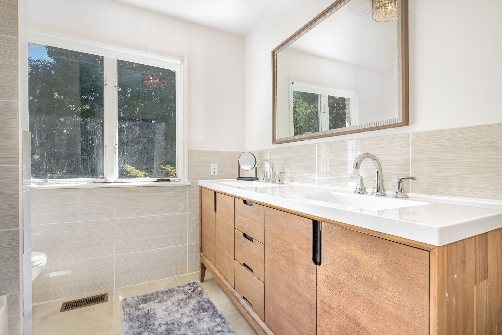 Une salle de bain moderne avec deux lavabos, un grand miroir et une fenêtre.