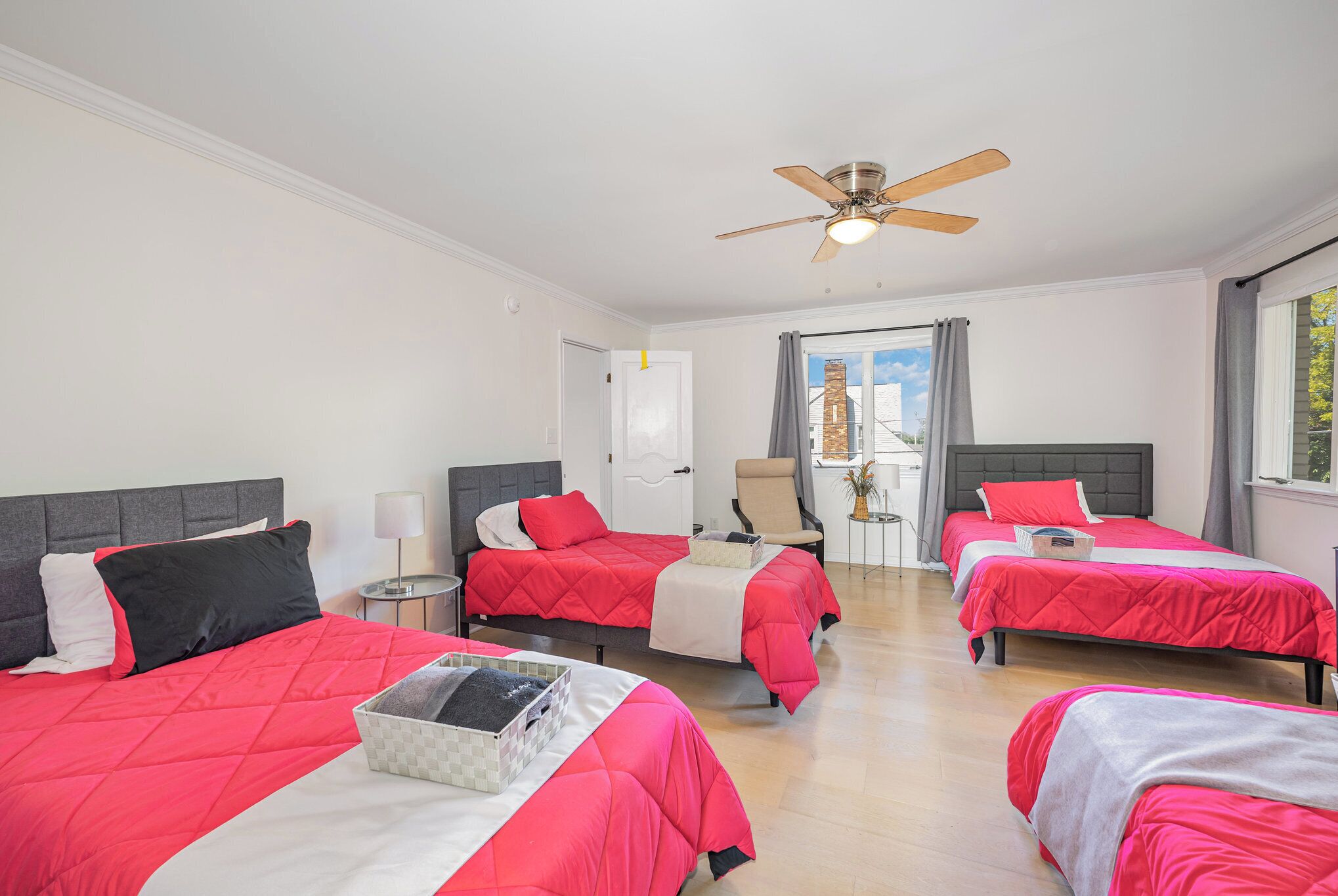 A hotel room with four beds, a ceiling fan, a window with curtains, and a door.