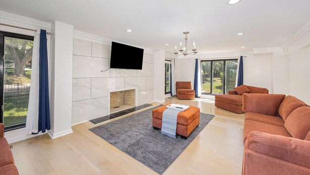 A modern living room with a fireplace, a flat-screen TV mounted on the wall, and a large window offering a view of the outdoors. - Spacious 4-bedroom house in Xenia near Universities (Xenia)
