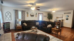 A living room with a sectional sofa, a coffee table, a fireplace, a ceiling fan, and a bookshelf.