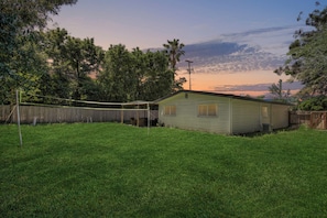A single-story house with a fenced backyard, a volleyball net, and a wooden deck.