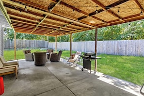 A covered patio with a concrete floor, wicker furniture, a grill, and a wooden ceiling.