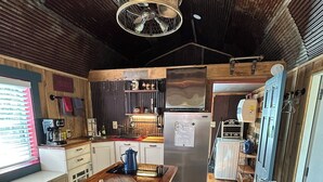 Une cuisine avec un îlot central en bois, des tabourets de bar, un réfrigérateur et un luminaire suspendu.
