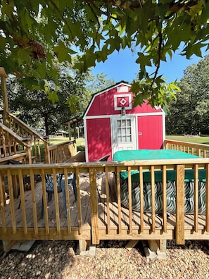 A red wooden structure with a green roof, surrounded by a wooden deck and gravel ground.