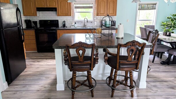 A kitchen with wooden cabinets, a black refrigerator, a granite countertop island, and two wooden bar stools. - 3-bedroom Private Forest Retreat Home with Wifi and Full Kitchen (Spring Hill)