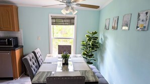 A dining area with a long table, cushioned chairs, a ceiling fan, and a window with blinds. - 3-bedroom Private Forest Retreat Home with Wifi and Full Kitchen (Spring Hill)