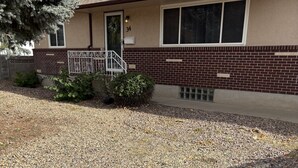 A single-story building with a brick facade, a front door, and a small porch with a metal railing. - The Loyola – Warm & Welcoming Home Base for Your Pueblo Adventure (Pueblo)
