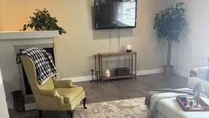 A living room with a fireplace, a yellow armchair, a grey sofa, a wooden console table, and a television mounted on the wall. - The Loyola – Warm & Welcoming Home Base for Your Pueblo Adventure (Pueblo)