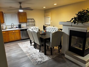 A modern kitchen with a dining area, wooden cabinets, a built-in oven, and a fireplace.