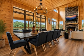 A wooden interior with a dining area, fireplace, and large windows. - Available XMAS!! Amazing Views+Pool+Pickleball+Upgraded Arcade+Theater+Hot Tub (Sevierville)