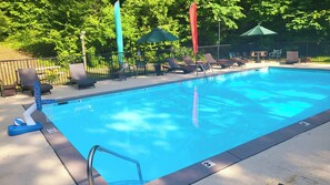 A swimming pool with lounge chairs and umbrellas, surrounded by a fence and trees.