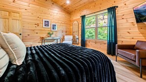 Une pièce chaleureuse, aménagée dans un chalet en bois, avec un lit, une chaise, une table et une fenêtre avec des rideaux.