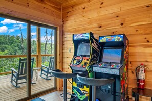 A wooden cabin with two arcade machines, rocking chairs, and a fire extinguisher.