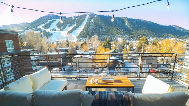 A balcony with a sofa, a table, and a view of a ski slope. - Bella's Mountain Vista | Prime Walk-to-Town 1BR Condo in Jackson Hole (Jackson)