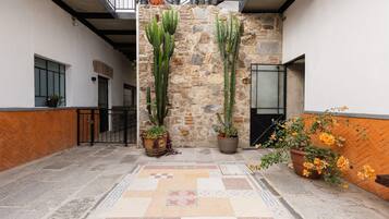 A courtyard with a stone wall, potted plants, a tiled floor, and a metal gate.