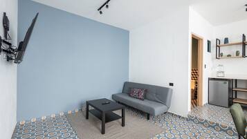 A modern living room with a grey sofa, a small black table, patterned floor tiles, and a ceiling-mounted light fixture.