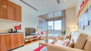 Ein modernes Hotelzimmer mit einer Küchenzeile, einem Flachbildfernseher, einem Sofa und einem großen Fenster mit Blick auf die Stadt.