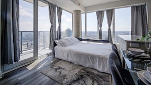 A modern hotel room with a large bed, a dining area, and a view of the city.