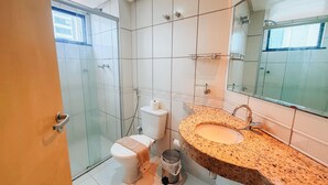 Une salle de bain moderne avec une douche à parois de verre, des toilettes avec un porte-serviettes et un lavabo doté d’un plan de travail en granit.