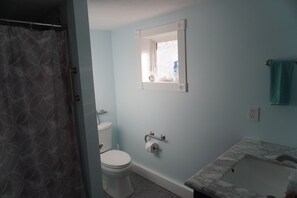 A bathroom with a toilet, a sink with a marble countertop, a towel hanging on the wall, and a shower curtain.