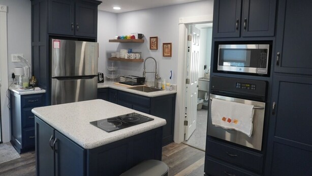 A modern kitchen with dark cabinets, stainless steel appliances, a central island, and a microwave.